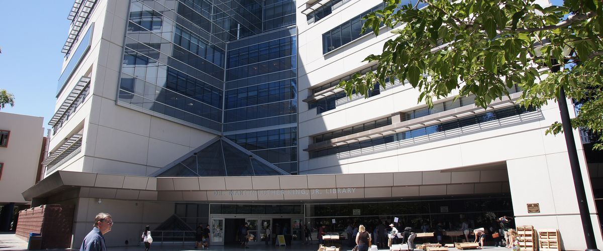 People walking past the glass entrance of the Dr. Martin Luther King Jr. Library in Downtown San Jose, home to several free library book clubs