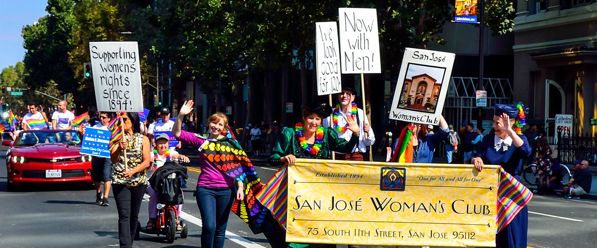 Marchers carrying signs and a banner down a tree-lined Downtown San Jose street during the Silicon Valley Pride Parade