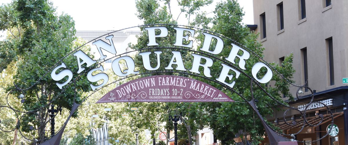 The arched San Pedro Square sign over a tree-lined street in Downtown San Jose, with a banner for the Friday farmers market