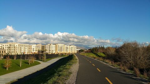Paved Guadalupe River Trail in San Jose curving past grass and trees under a blue sky, a common route for group runs
