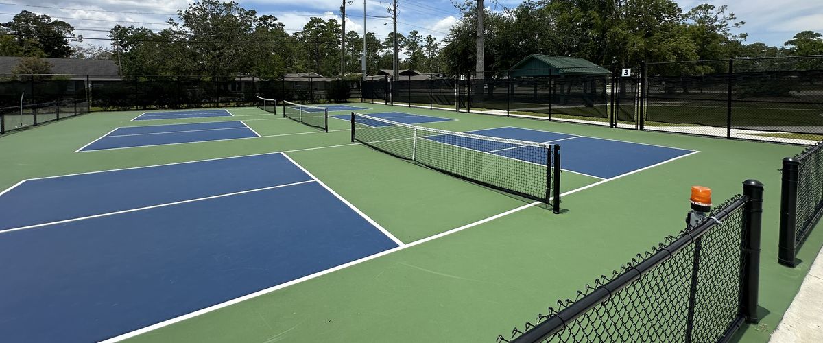 Row of blue and green outdoor pickleball courts with nets set up for play on a sunny day